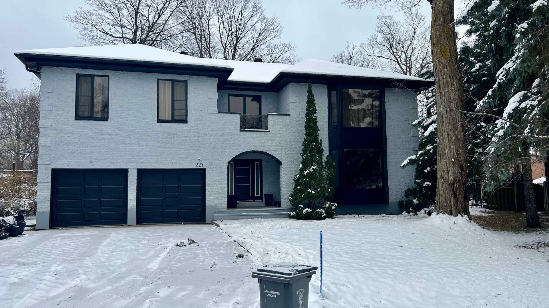 A large white house with black garage doors is covered in snow.