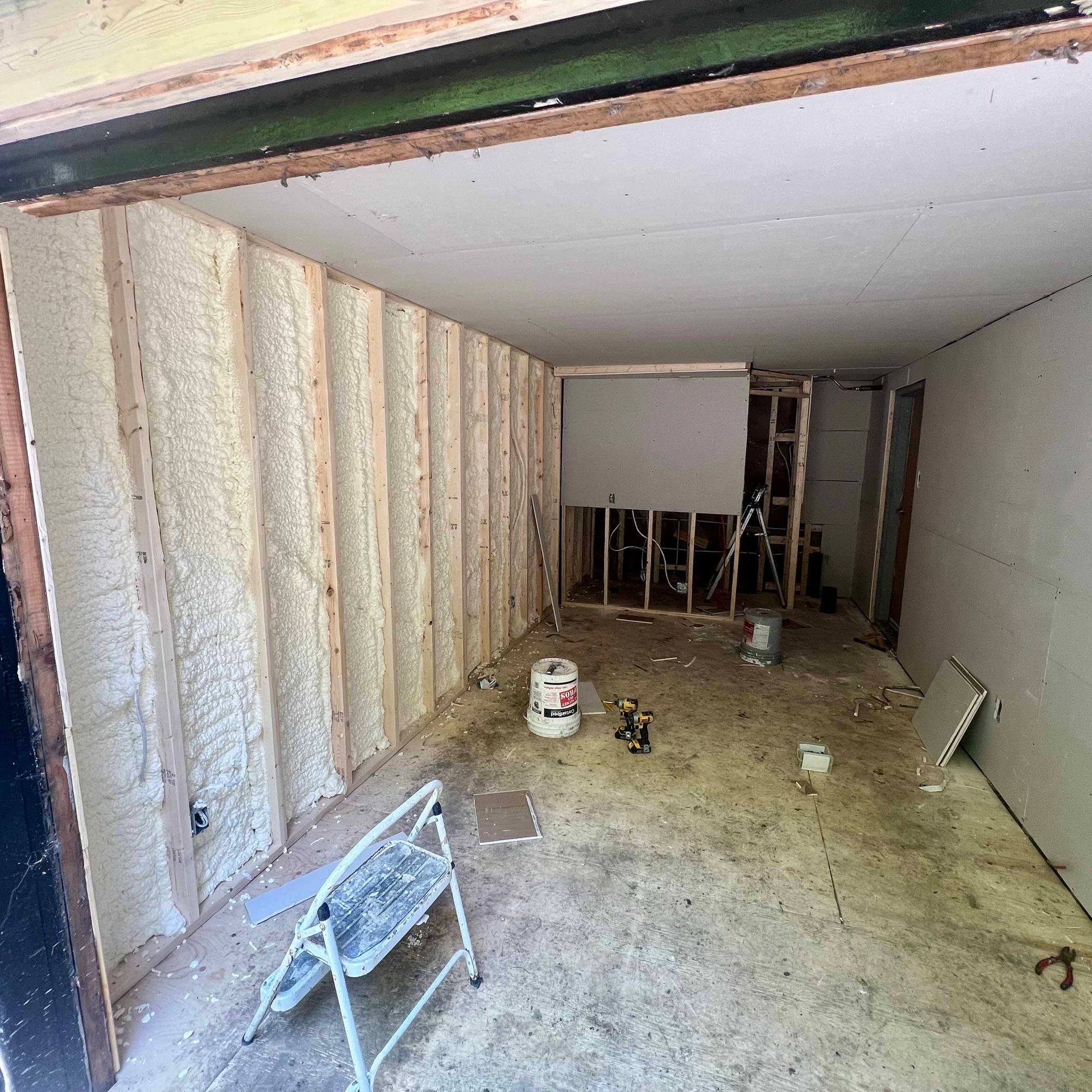 A room with a ladder and a bucket of paint in it.