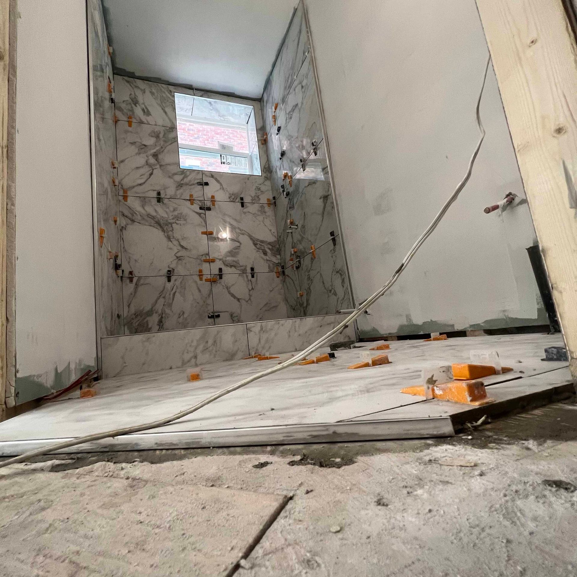 A bathroom under construction with tiles on the floor and a window.