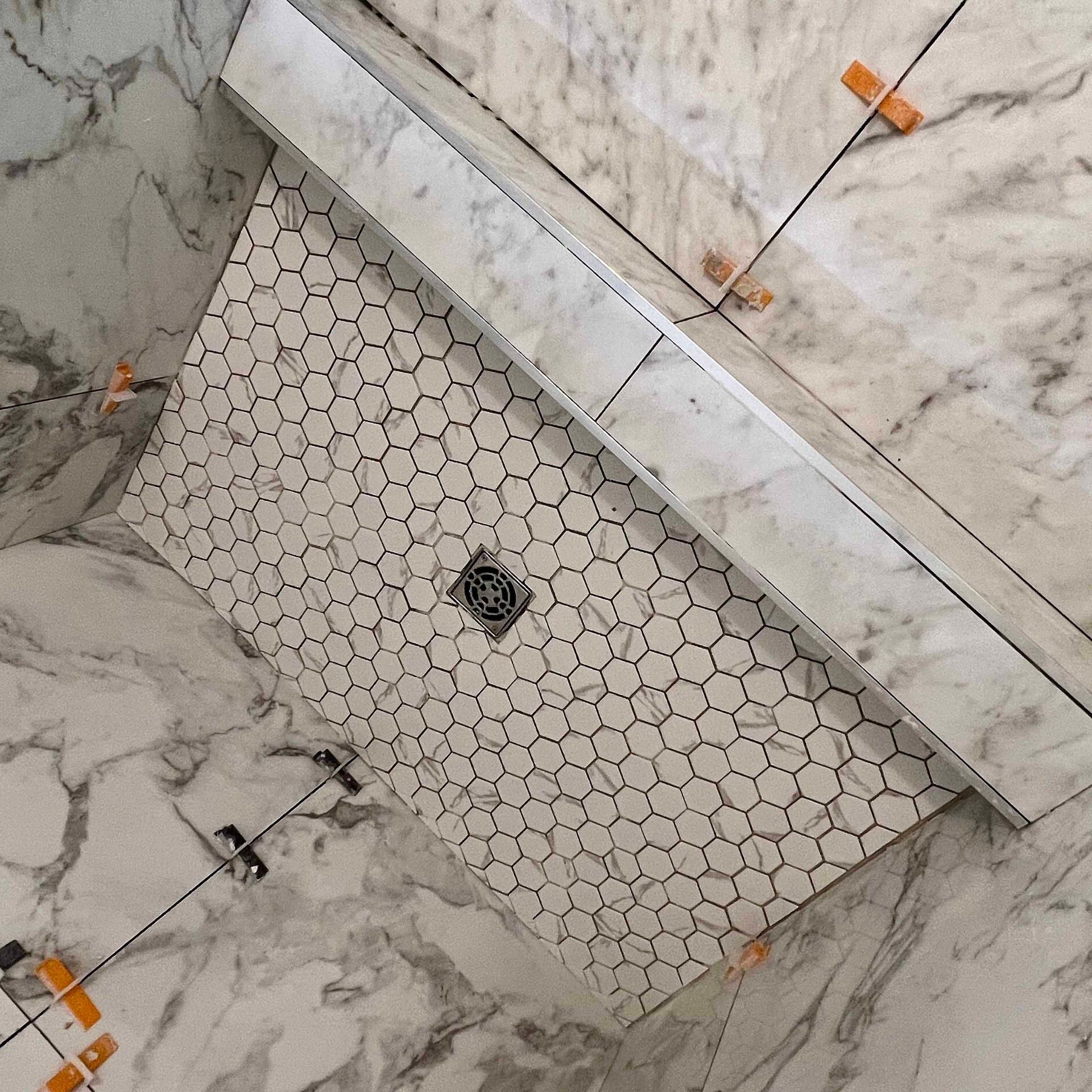 A shower stall with a hexagonal tile floor and a drain.