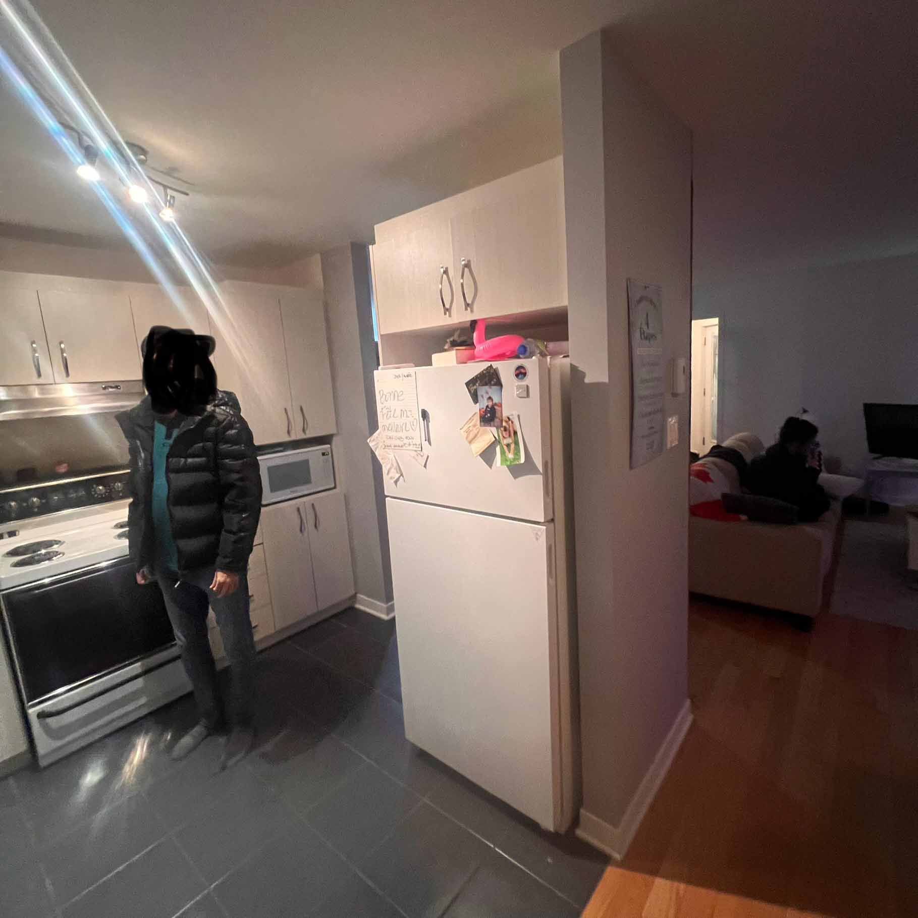 A man is standing in a kitchen next to a refrigerator.
