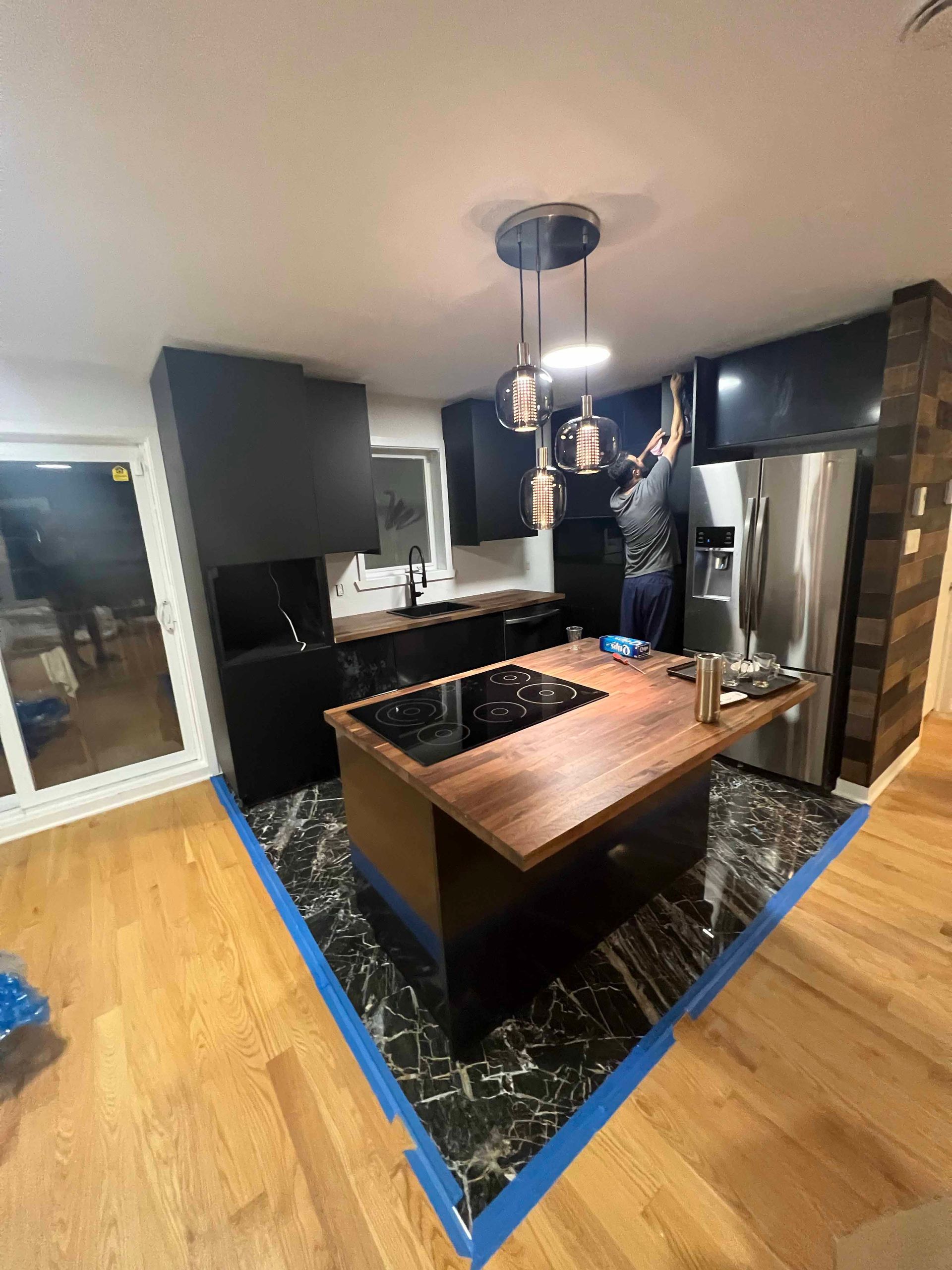 A man is working on a kitchen with black cabinets and a wooden island.