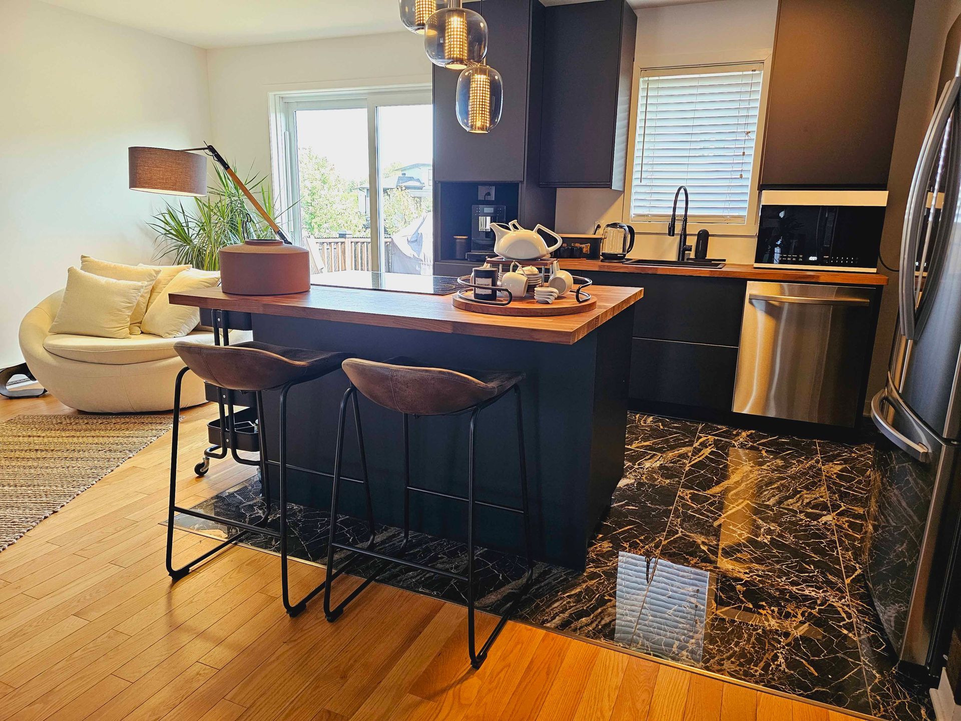 Modern kitchen with island, seating, and stainless steel appliances, open to living area with white chair.