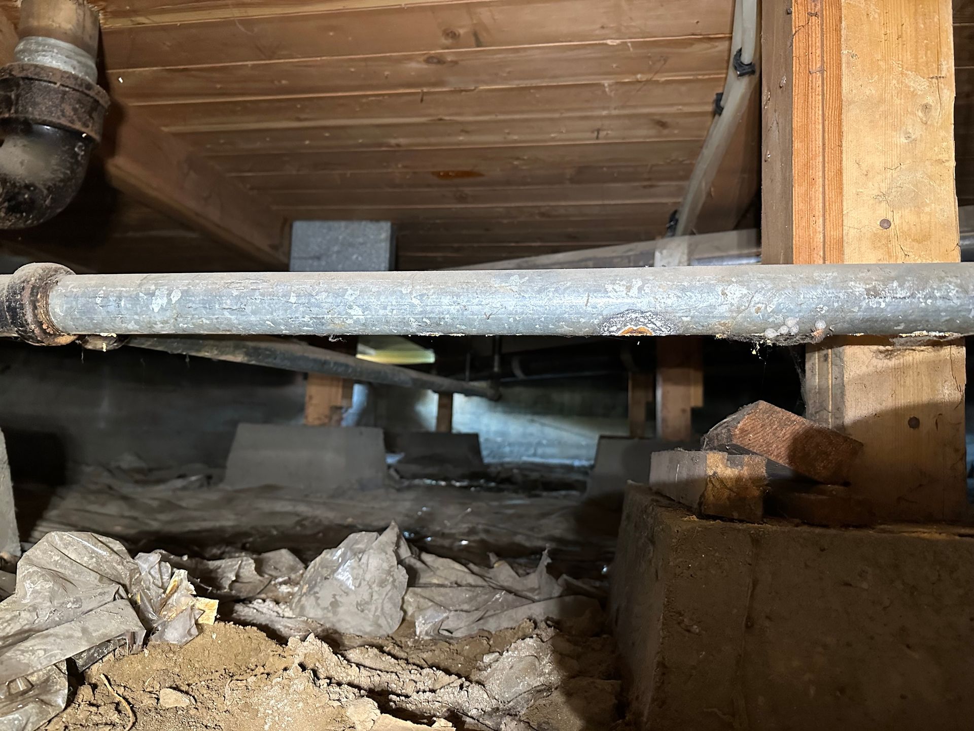 A pipe is sitting under a wooden ceiling in a basement.