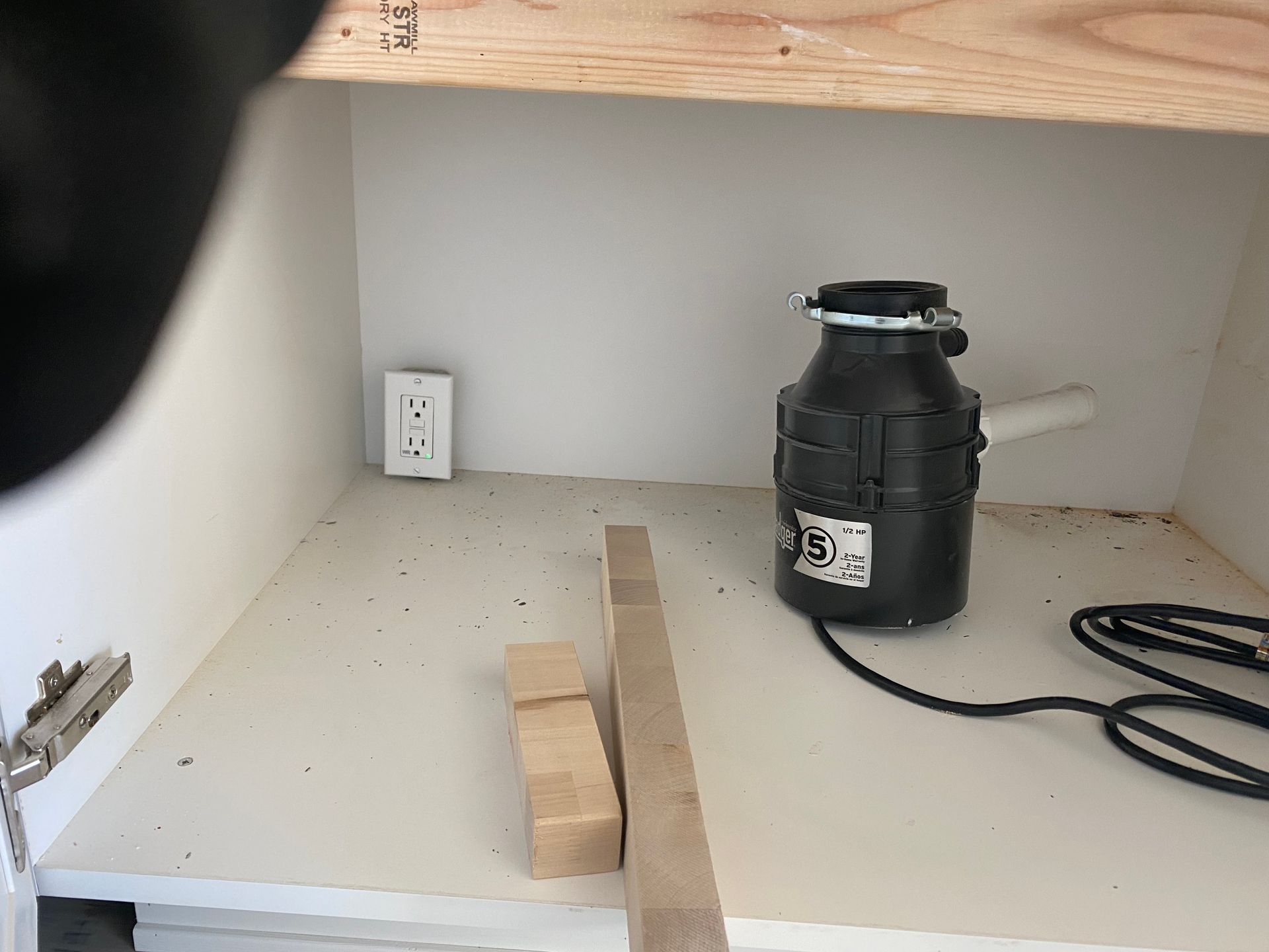 A garbage disposal is sitting inside of a kitchen cabinet.