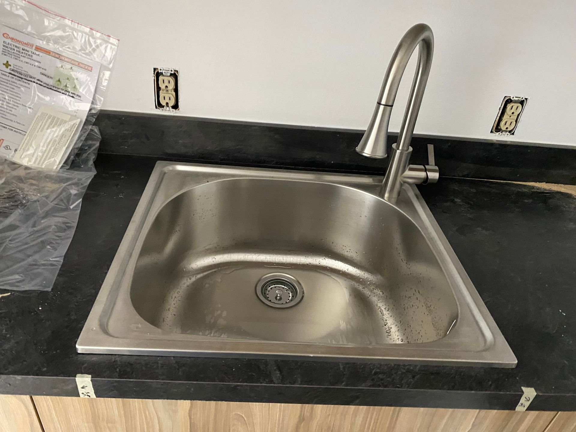 A stainless steel sink with a faucet on a black counter top.