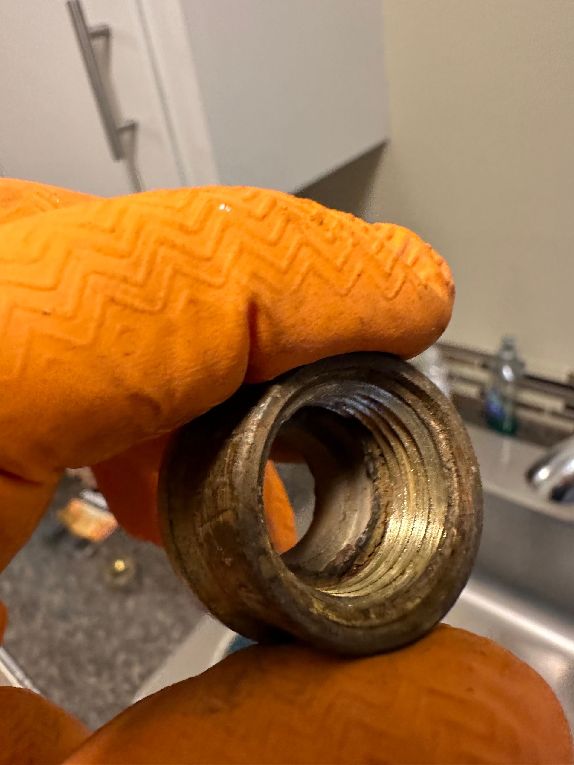 A person wearing orange gloves is holding a metal nut in their hand.