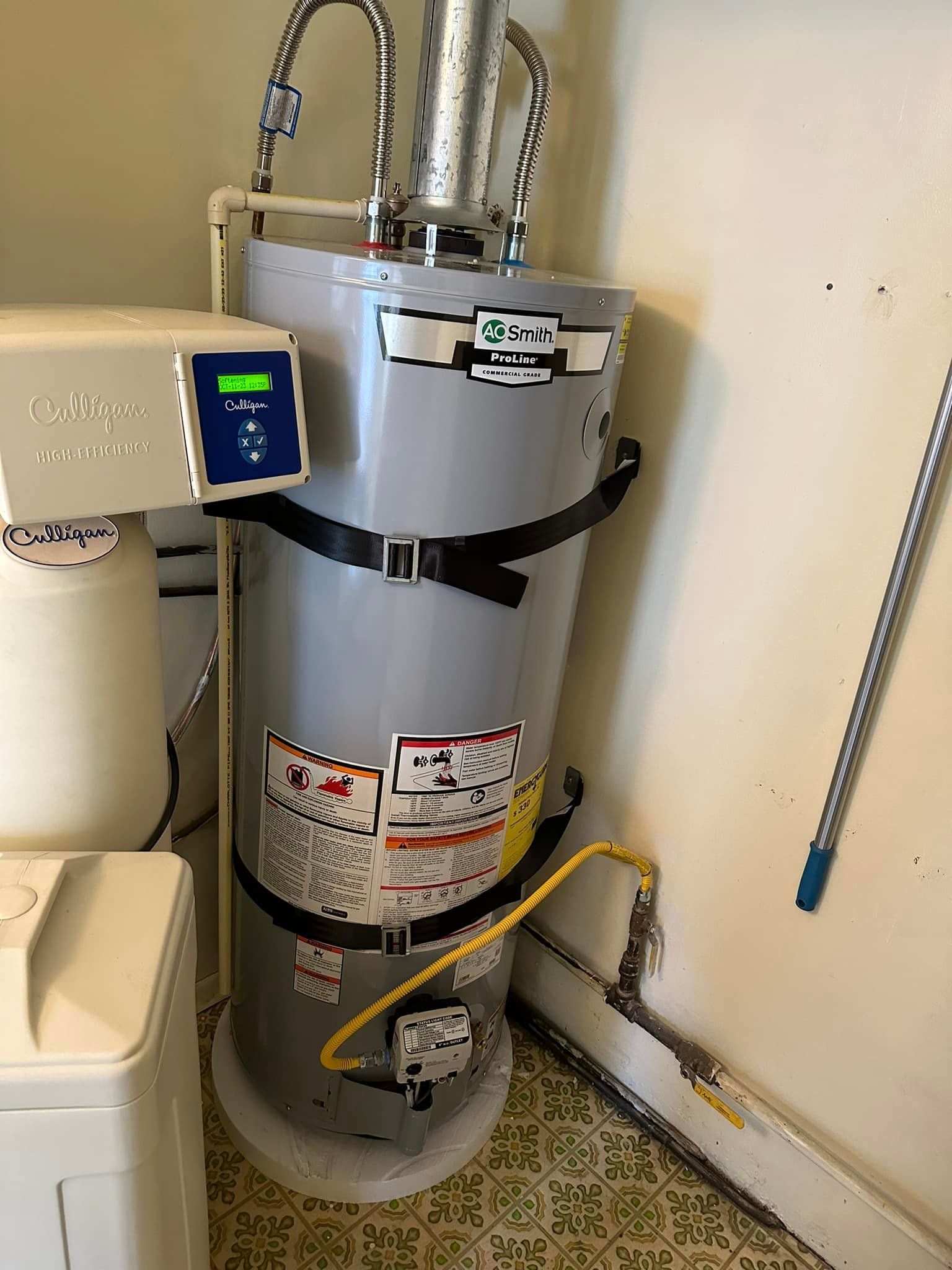 A water heater is sitting in a corner of a room next to a washer and dryer.