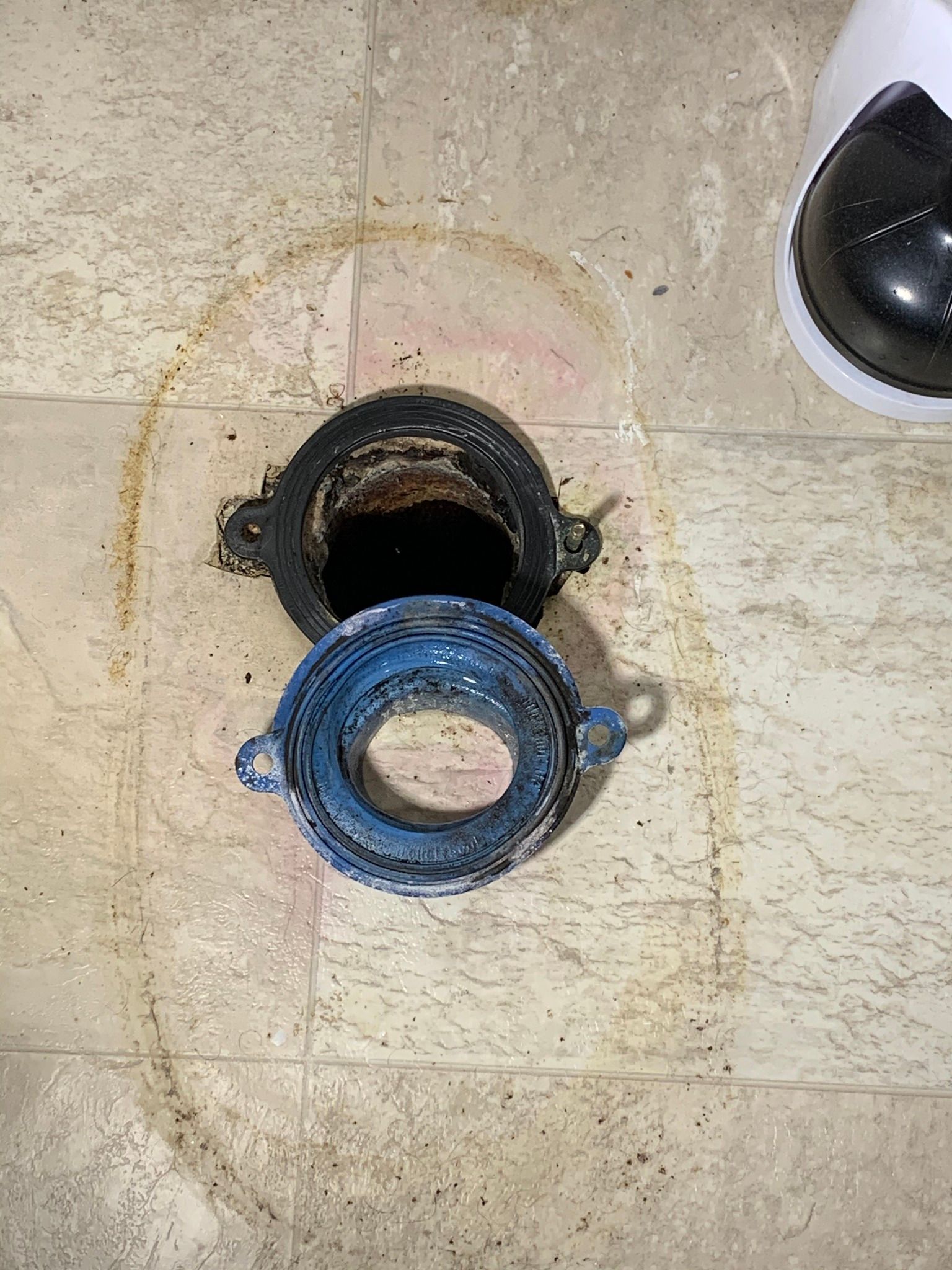 A close up of a toilet flange on a tiled floor.