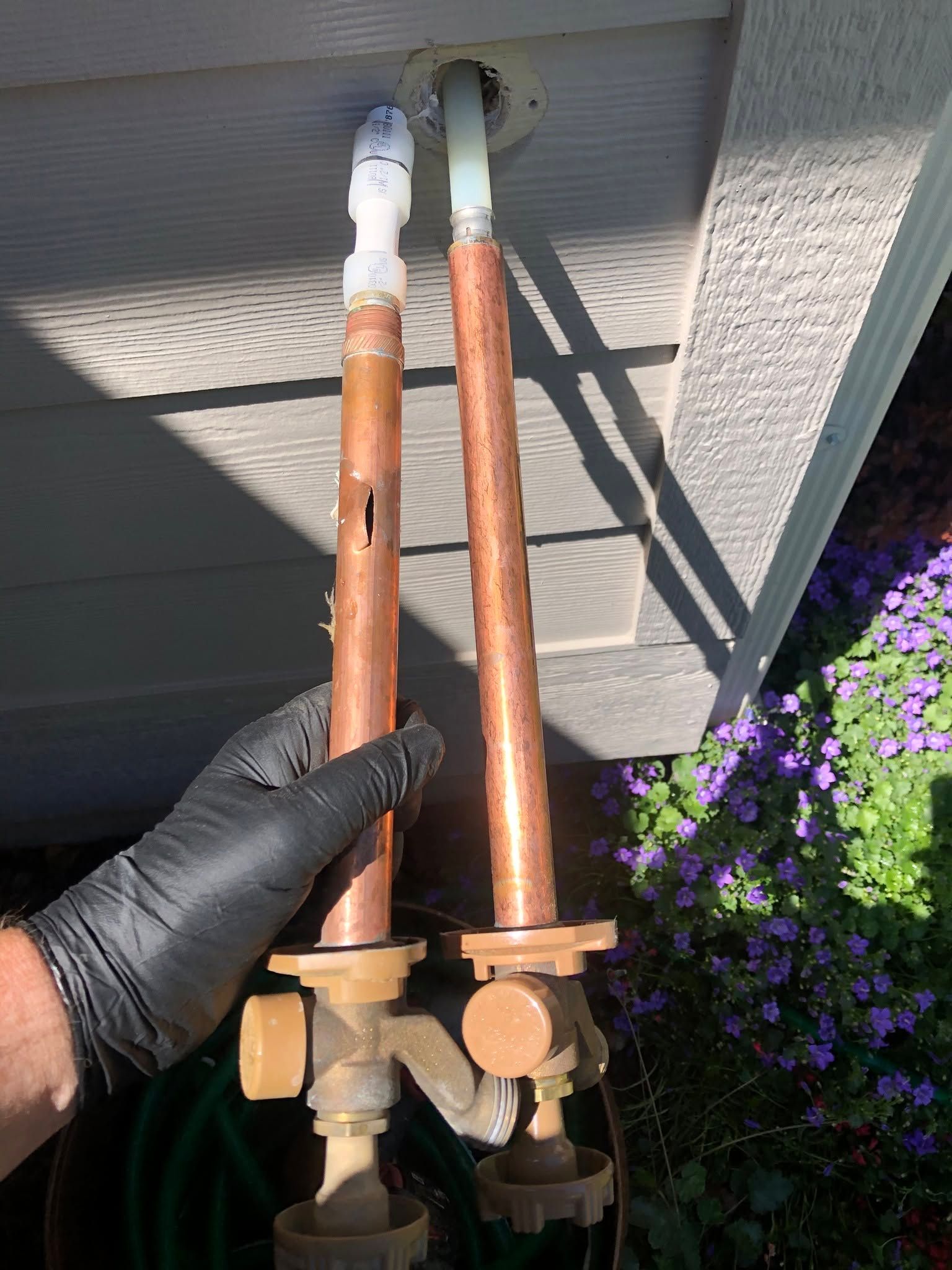 A person is holding two copper pipes next to a house.