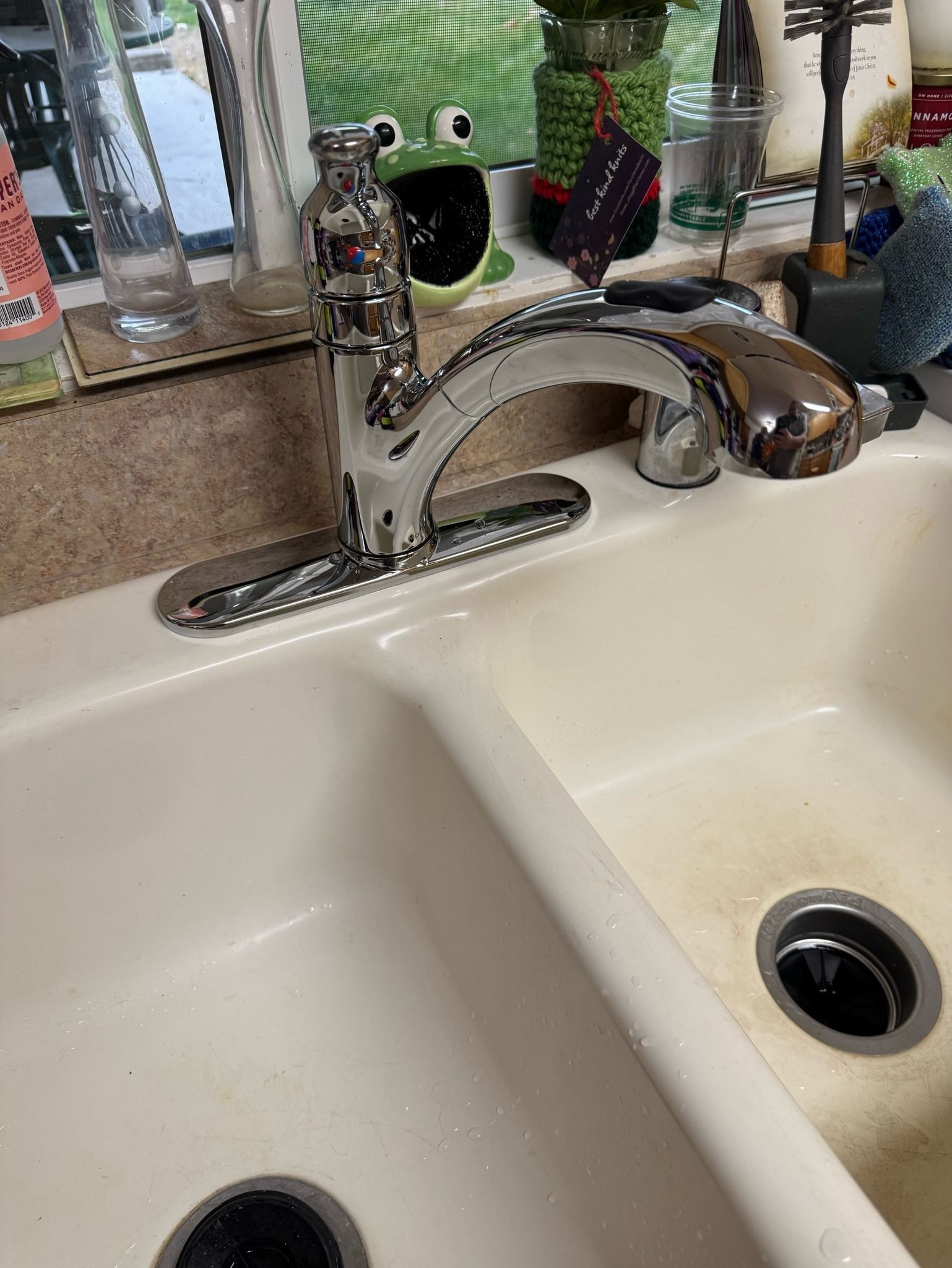 A close up of a kitchen sink with a frog on the counter.