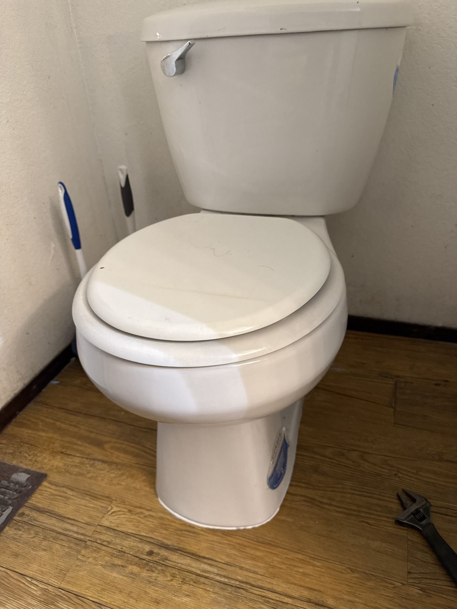 A white toilet is sitting on a wooden floor in a bathroom.