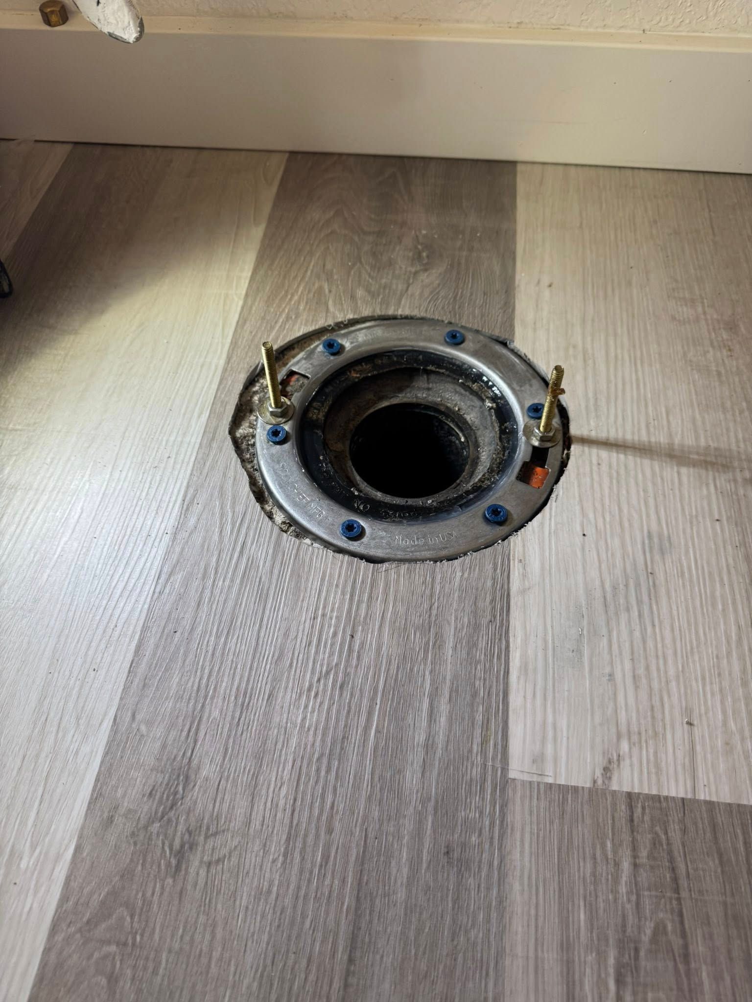 A hole in the floor of a bathroom with a metal flange attached to it.