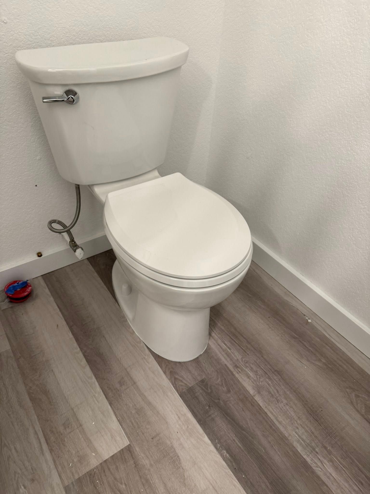 A white toilet is sitting on a wooden floor in a bathroom.