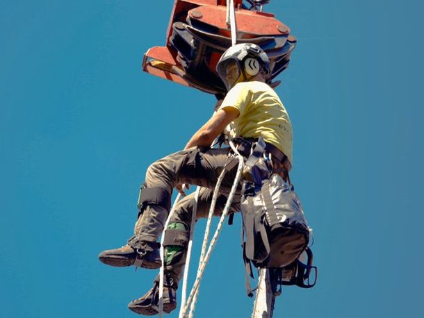 Man in safety gear on a crane, looking down; blue sky background.