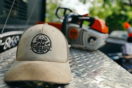 Tan hat with company logo sits on a metal surface with a chainsaw in the background.