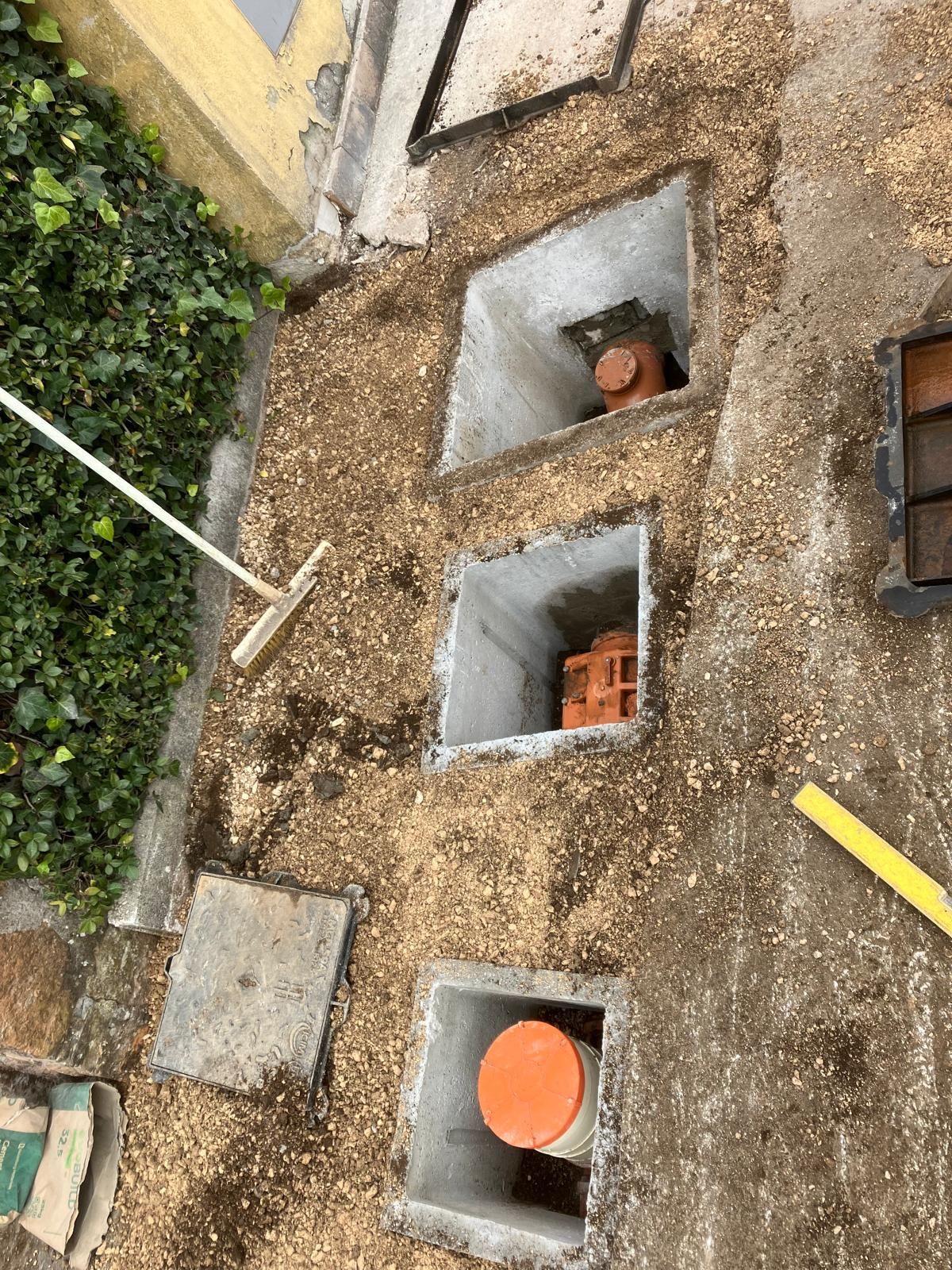 Vista dall'alto di tre cabine di servizio in cemento con coperchi arancioni, posizionate su ghiaia a lato di un sentiero in giardino.