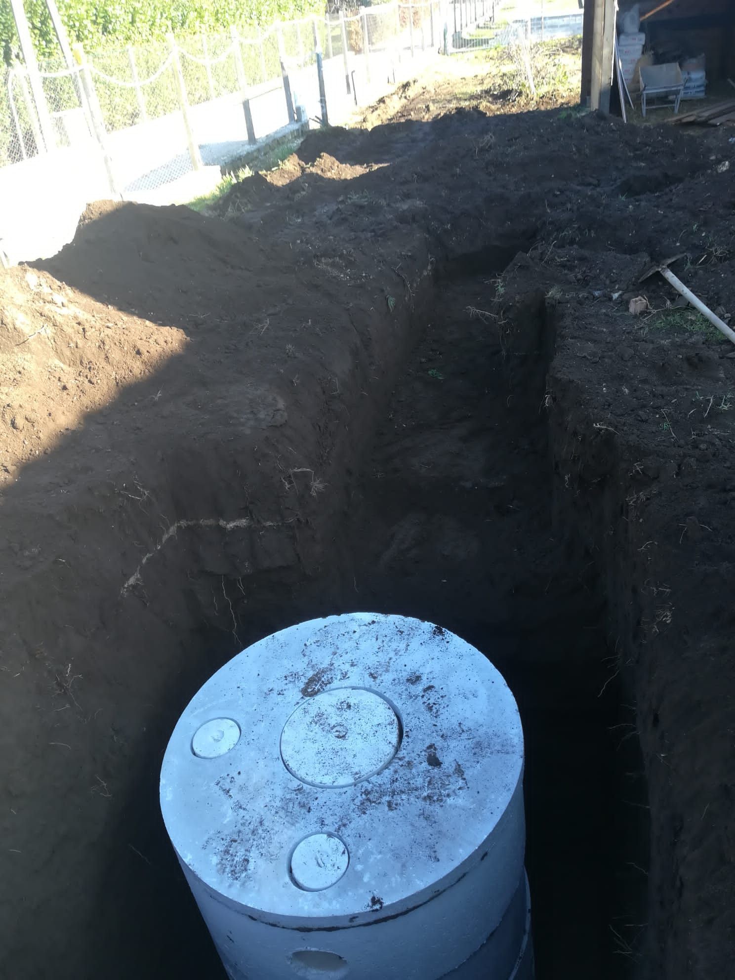 Scavo a cielo aperto con un coperchio di cemento circolare sul fondo, vicino a una recinzione.
