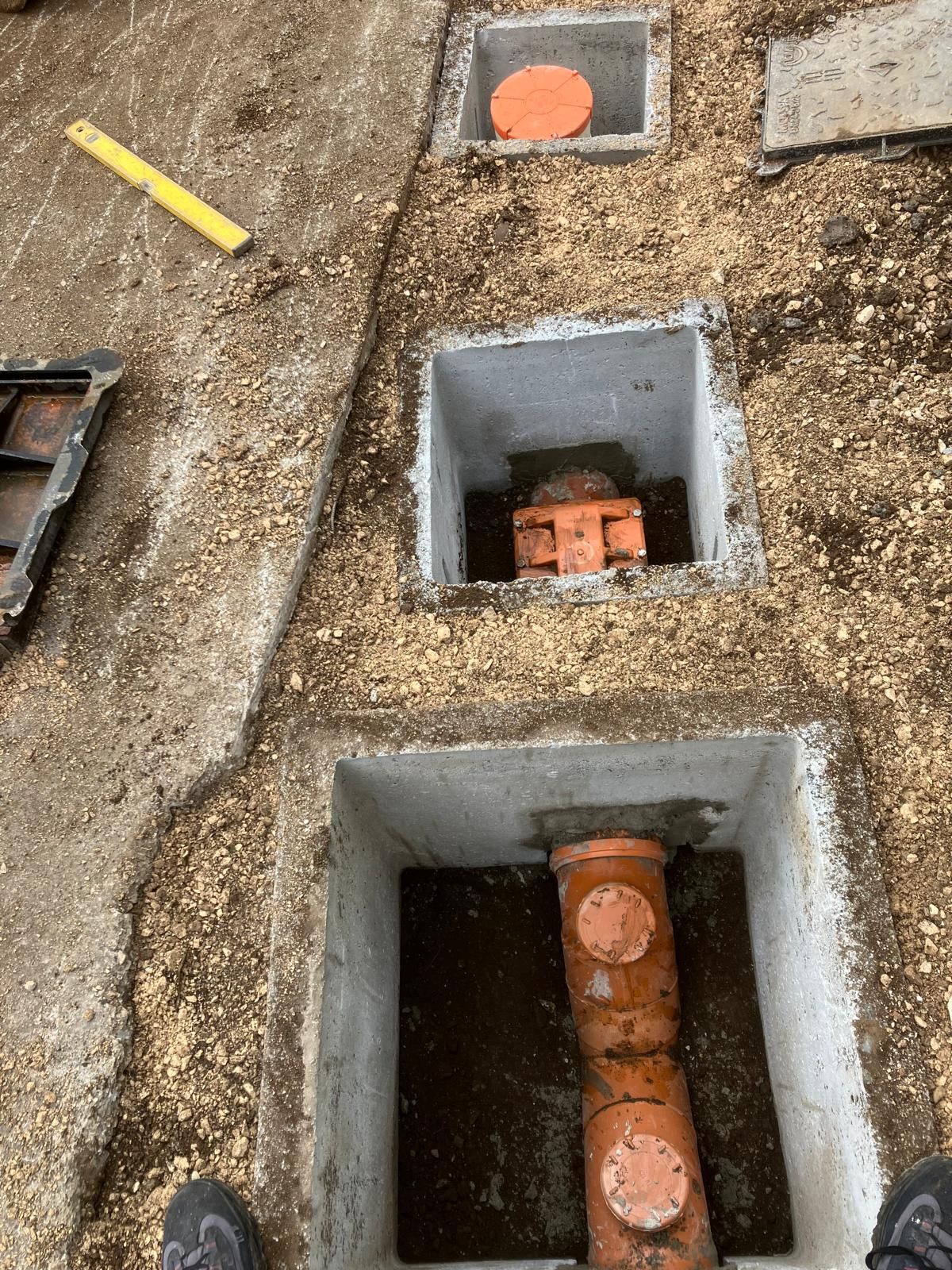 Scatole di derivazione aperte nella ghiaia con tubi arancioni a vista e un indicatore giallo nelle vicinanze.