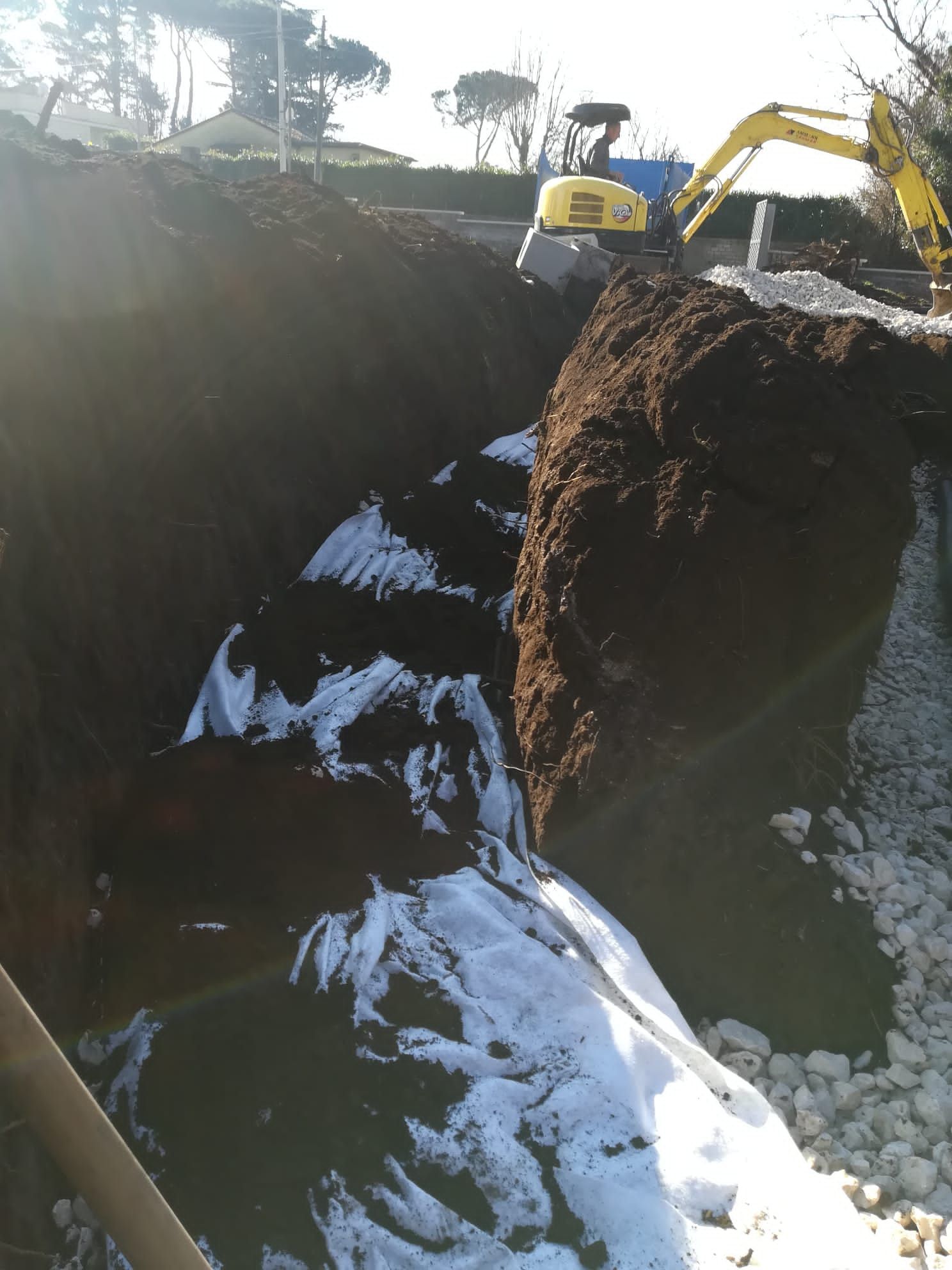 Escavatore che scava una grande trincea con terreno esposto e neve sul fondo.