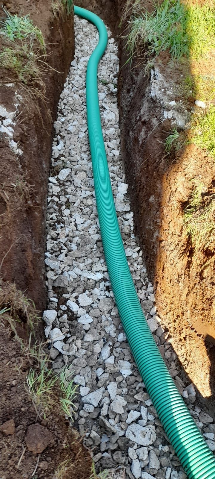 Tubo corrugato verde posato in una stretta trincea con ghiaia e terra intorno