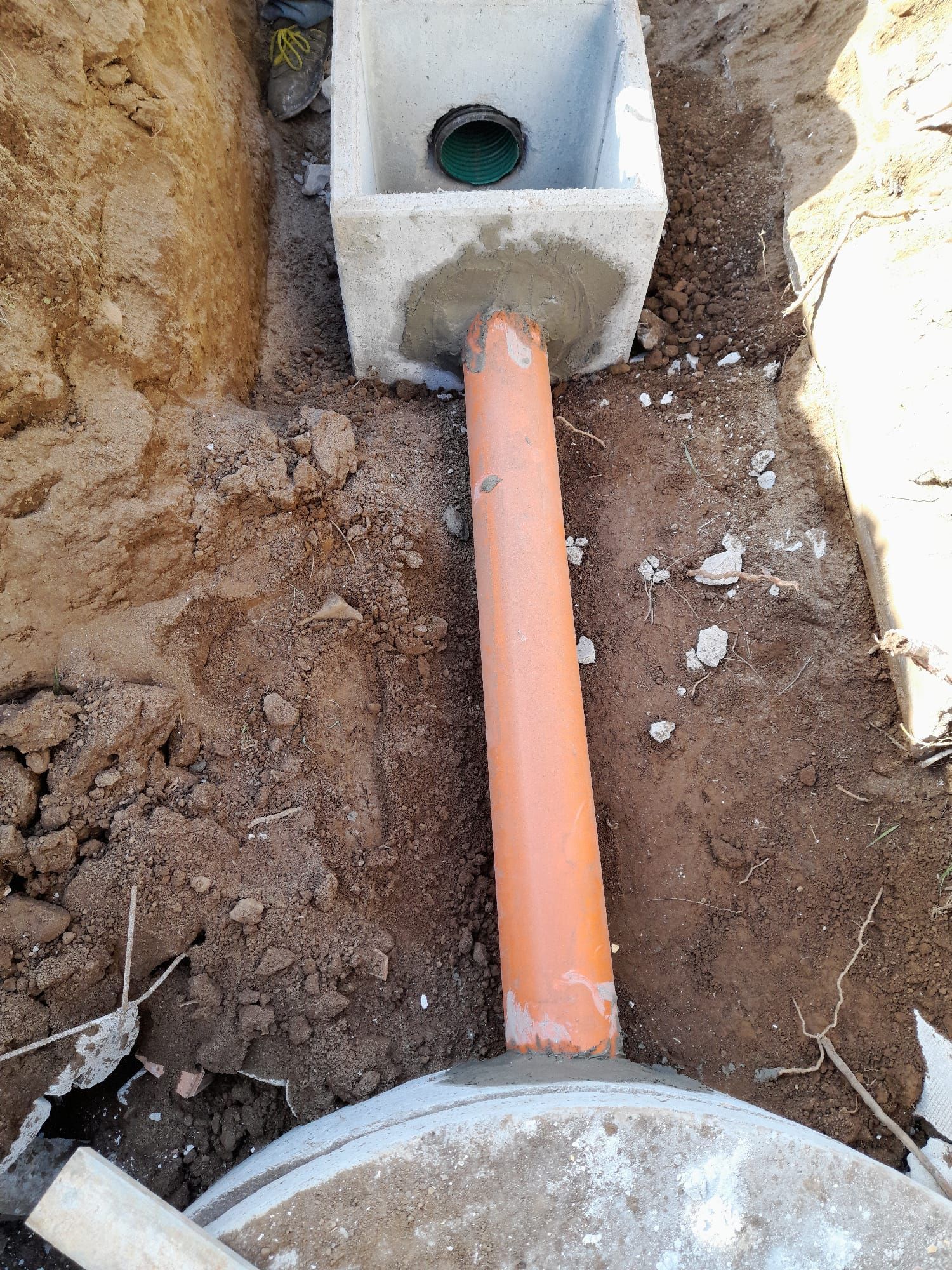 Tubo arancione collegato a una scatola di drenaggio in cemento in una trincea di terra