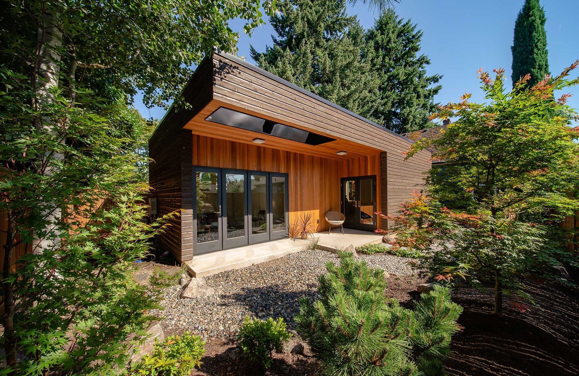 A small wooden house with a lot of windows is surrounded by trees.