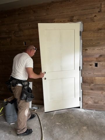 Worker installing a white door in a wood-paneled room