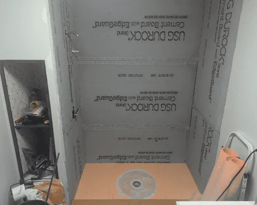 Shower enclosure under construction with grey USG Durock cement board walls and a pre-sloped foam shower pan base.