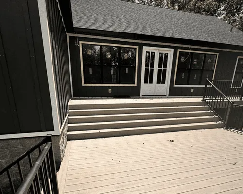 A set of wide concrete steps leads up from a light-colored wooden deck to the white French doors of a dark-sided house.
