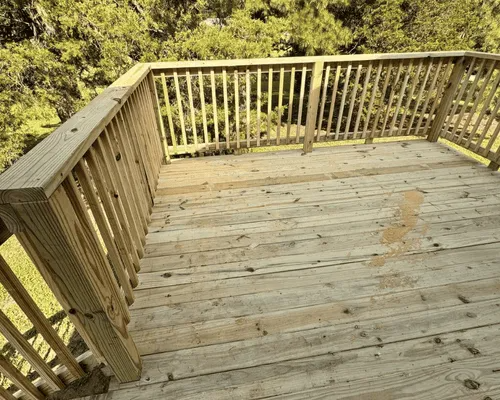 A high-angle view of a wooden deck with railing, overlooking a lush green yard with trees.