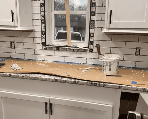 A kitchen renovation in progress, featuring white subway tile backsplash, a window, granite countertops, and white cabinets.
