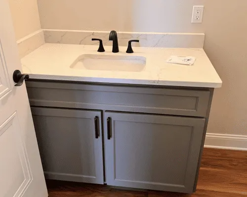 A grey bathroom vanity with a white marble-patterned countertop, a rectangular sink, and matte black hardware.