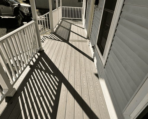 A light-colored porch with white railings, featuring dramatic diagonal shadows cast across the deck boards.