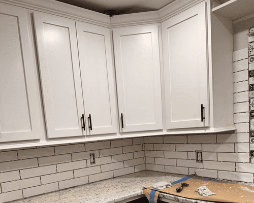 White Shaker-style kitchen cabinets installed above a granite countertop with white subway tile backsplash.
