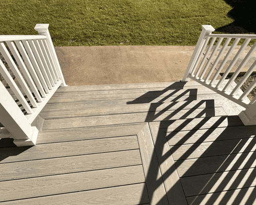 A high-angle view looking down at a gray composite porch deck with white railings, leading to a concrete walkway.