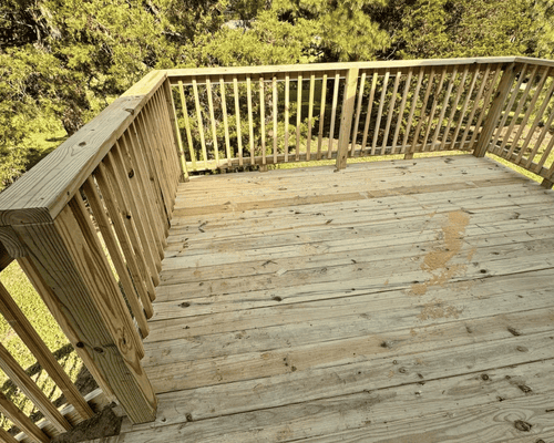 A wooden deck with railings overlooking a forest of green trees.