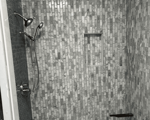 A shower with a modern handheld showerhead, a wall niche, and rectangular stone tile in a vertical stacked pattern.