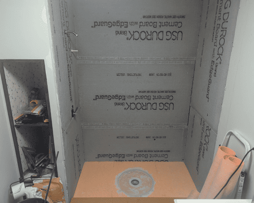 A shower renovation in progress with grey Durock cement boards installed on the walls and an orange foam shower base.