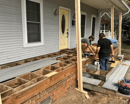 Two workers installing new gray composite decking boards on a residential porch frame.