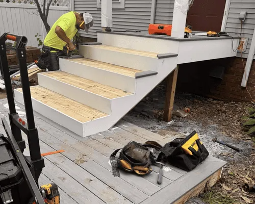 A worker in a high-visibility yellow shirt uses a power sander on newly installed wooden porch stairs.