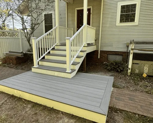 Gray composite deck and stairs with white railings in front of a light yellow house with light gray siding.