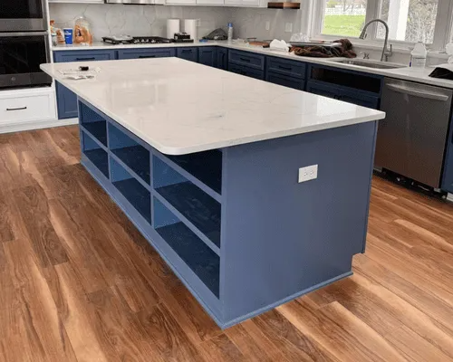 A large kitchen island with deep blue cabinets and open shelving, topped with a white quartz countertop on wood floors.