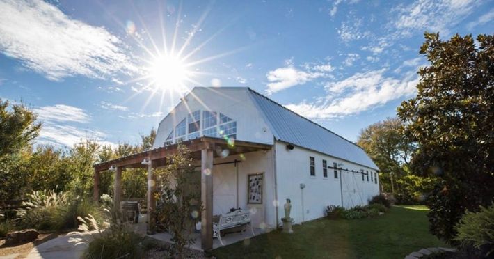 A white barn with a porch and the sun shining through the windows.