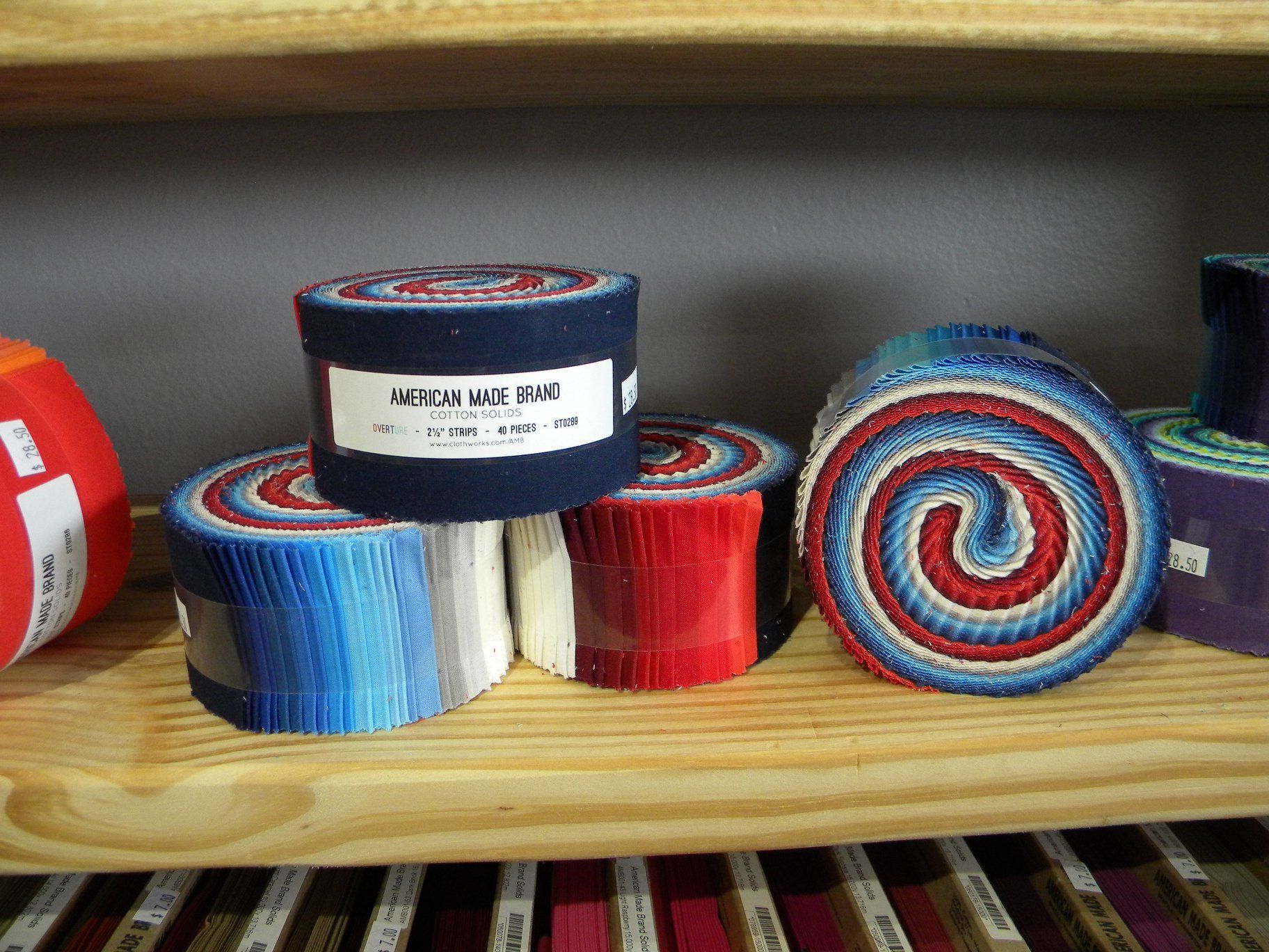 Coiled red, blue, and white striped fabric rolls on a wooden shelf.