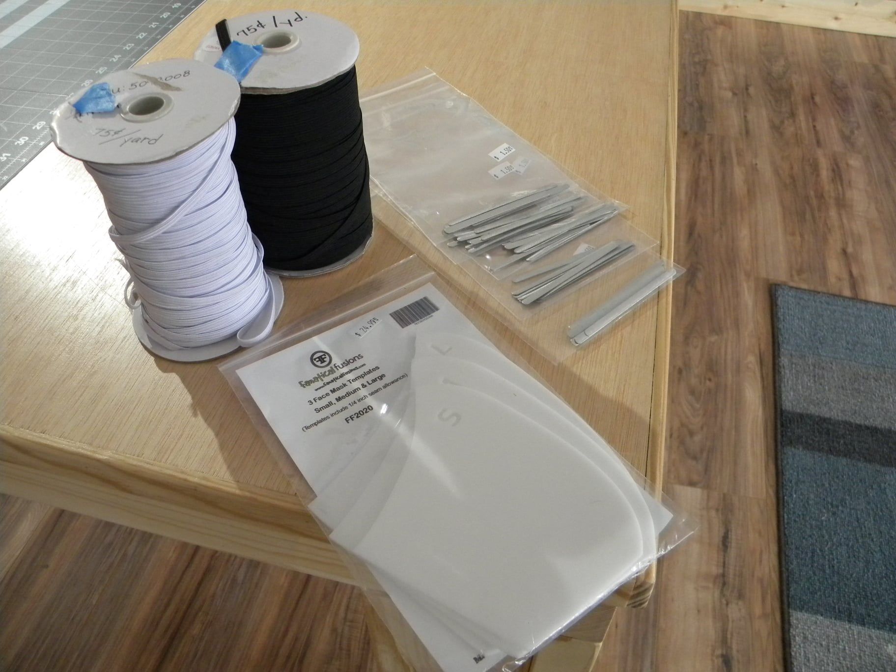 White and black thread spools, zippers, and a clear bag of sewing supplies on a wooden table