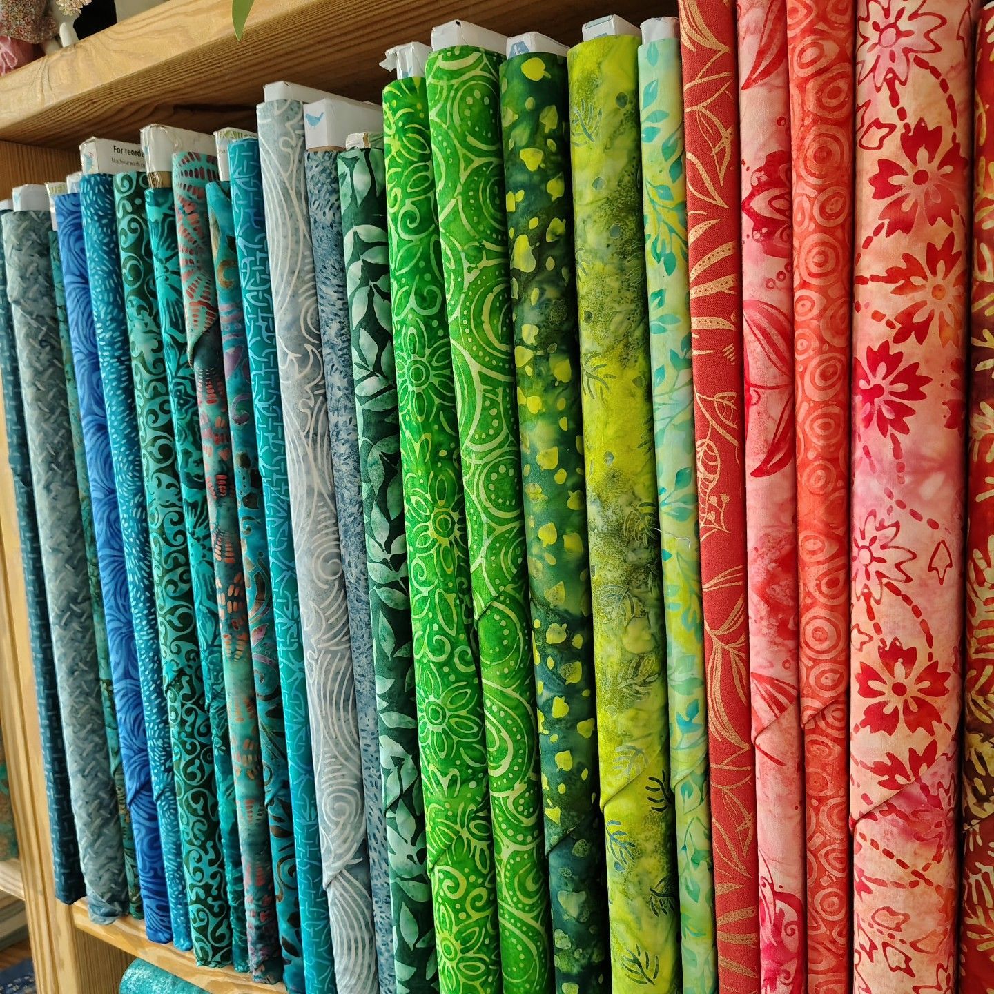 Rows of colorful rolled fabrics in blues, greens, and pinks on a shelf