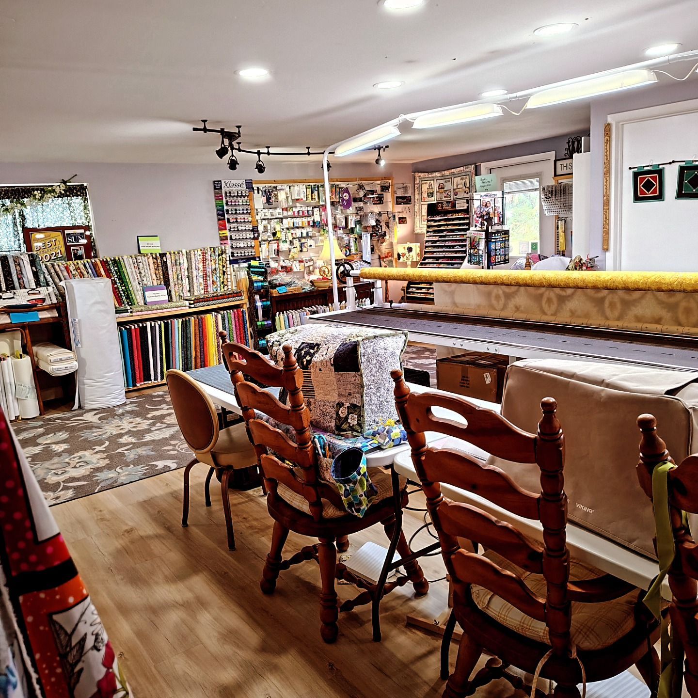 Cozy fabric shop with chairs at a counter, colorful bolts of fabric, and shelves of supplies in the background