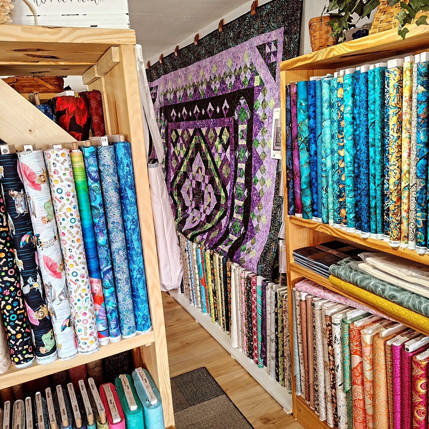 Fabric store shelves packed with colorful rolled quilting fabrics and a purple patterned wall hanging in the back