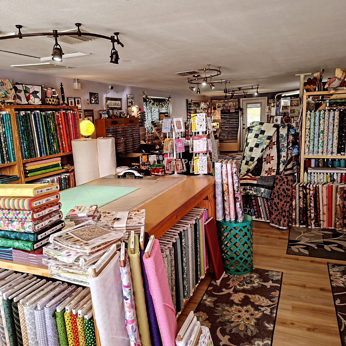 Fabric shop interior with colorful bolts of cloth, display tables, and patterned textiles throughout